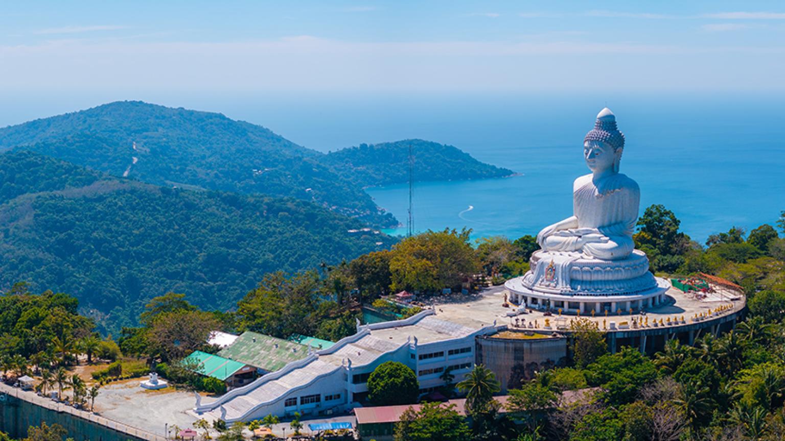 Vista Aéreas de la estatua del Gran Buda en una colina verde en Phuket, Tailandia, con senderos, estructuras circundantes y el mar de Andamán al fondo.