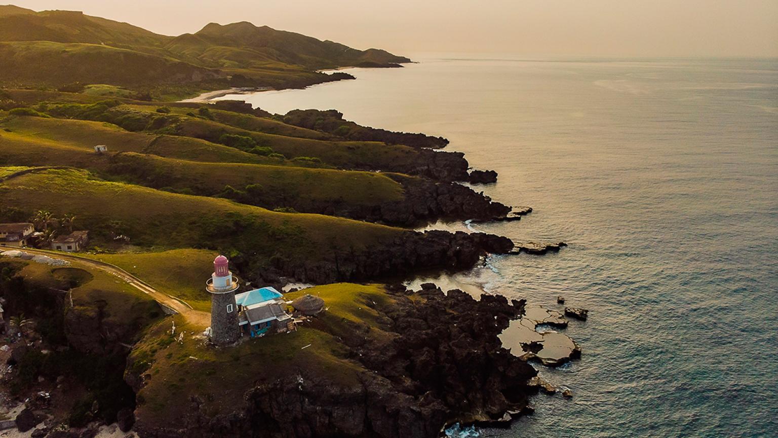 Una hermosa vista de las verdes colinas y la playa al atardecer en Batanes, Filipinas.