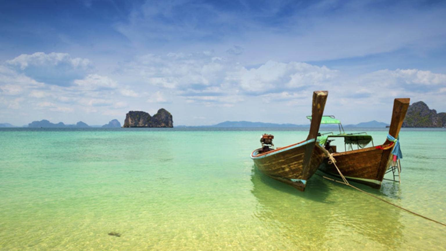 Barcos tradicionales tailandeses de cola larga varados en la playa, y al fondo, formaciones rocosas de caliza, en Trang, al sur de Tailandia