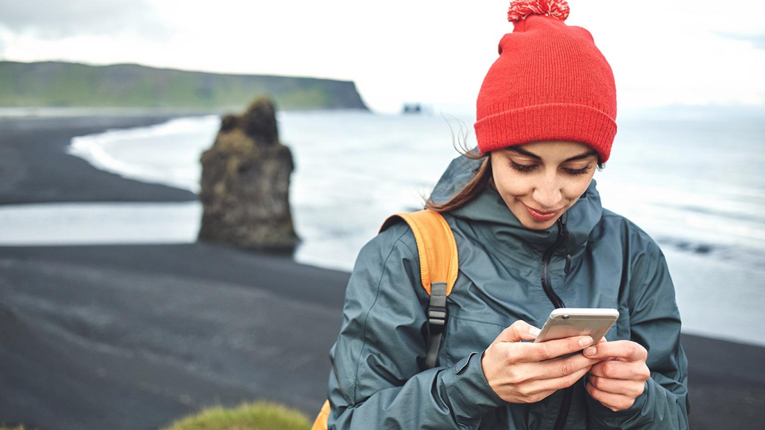 Viajera con smartphone en Kirkjufjara, Islandia