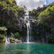 Full outdoor shot of a waterfall cascading down a rocky cliff face into a tranquil pool of emerald green water, Reunion